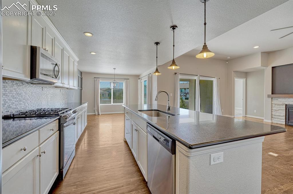 8437 Salt Brush Road Colorado Springs, CO 80908 - Photo 18 of 45 Bring your passion for cooking to life in this exceptional kitchen, boasting premium stainless steel appliances, elegant wood floors, a practical kitchen island with sink, sophisticated white cabinetry, and a stunning decorative backsplash that completes the look.