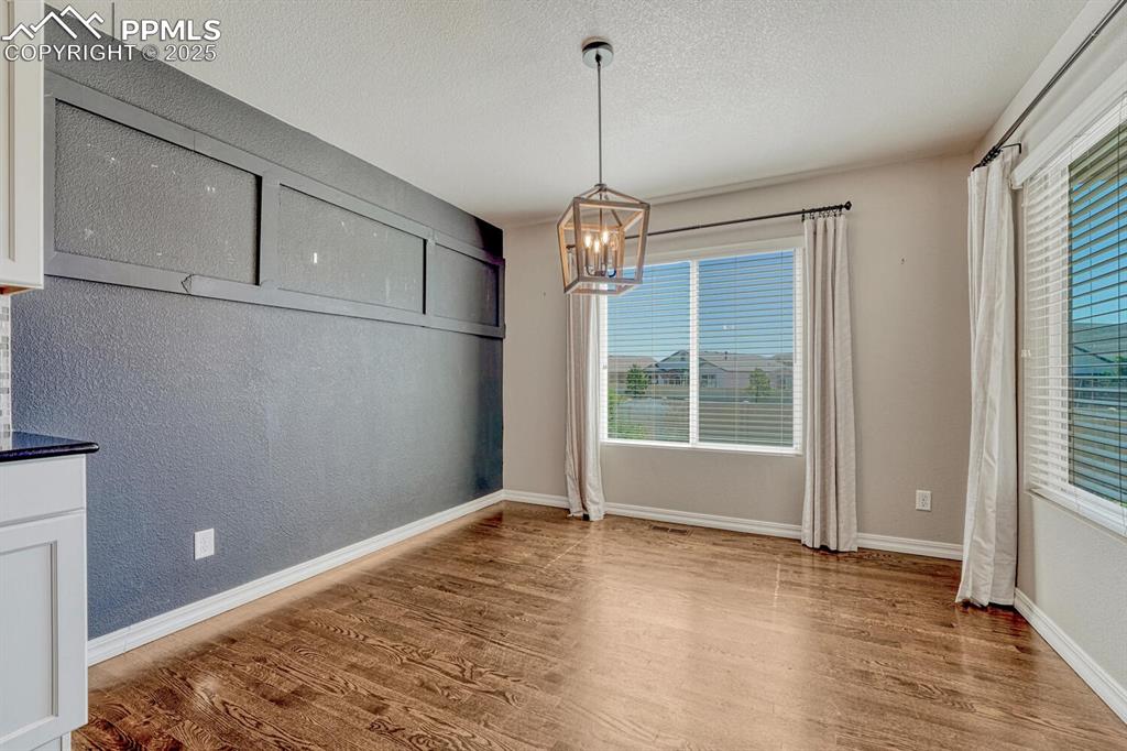 8437 Salt Brush Road Colorado Springs, CO 80908 - Photo 44 of 45 Experience a dining space that beautifully blends warmth and sophistication, showcasing rich wood floors, a magnificent chandelier, and intriguing textured details on walls and ceiling.