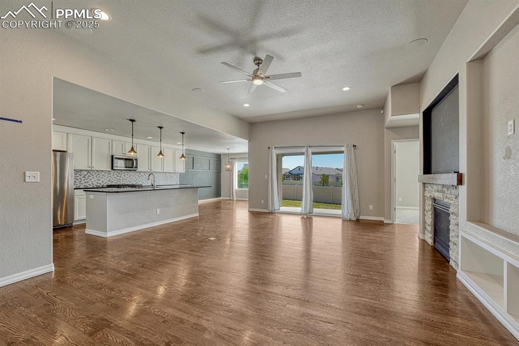 8437 Salt Brush Road Colorado Springs, CO 80908 - Photo 8 of 45 Step into the family room, where a ceiling fan, stone fireplace, and stunning wood floors converge to create a warm and inviting atmosphere, complete with a textured ceiling, walkout to the covered patio, and recessed lighting.