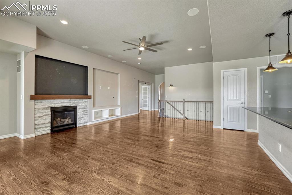 8437 Salt Brush Road Colorado Springs, CO 80908 - Photo 9 of 45 Step into the family room, where a ceiling fan, stone fireplace, and stunning wood floors converge to create a warm and inviting atmosphere, complete with a textured ceiling, walkout to the covered patio, and recessed lighting.