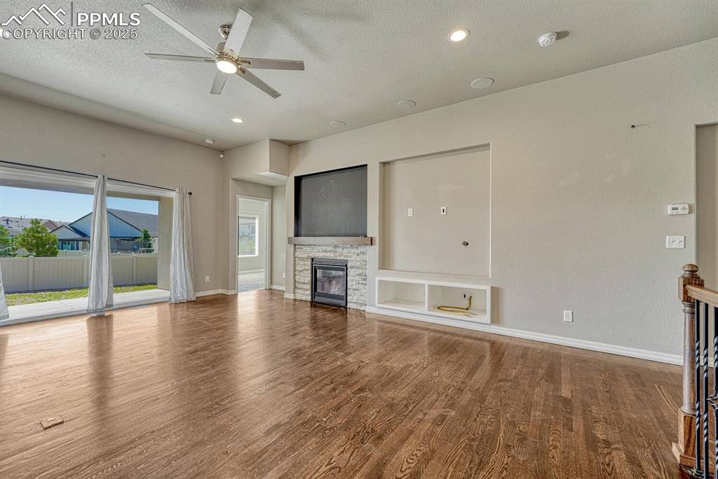 8437 Salt Brush Road Colorado Springs, CO 80908 - Photo 10 of 45 Step into the family room, where a ceiling fan, stone fireplace, and stunning wood floors converge to create a warm and inviting atmosphere, complete with a textured ceiling, walkout to the covered patio, and recessed lighting.