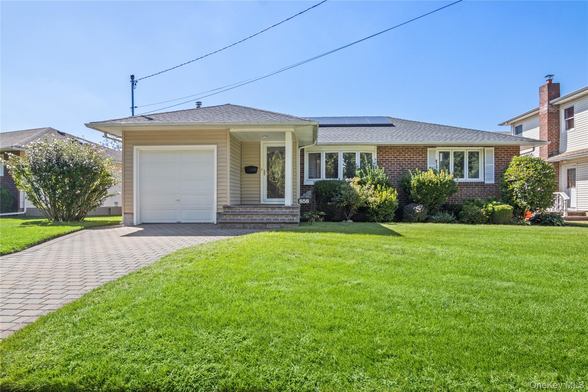 Ranch-style home with roof mounted solar panels, an attached garage, decorative driveway, and a front yard