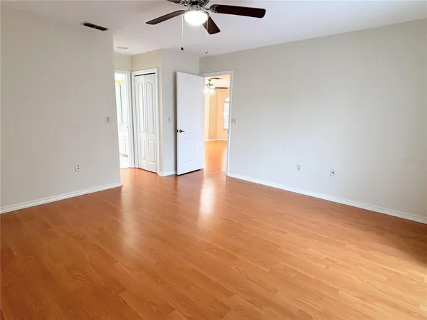 an empty room with wooden floor fan and windows