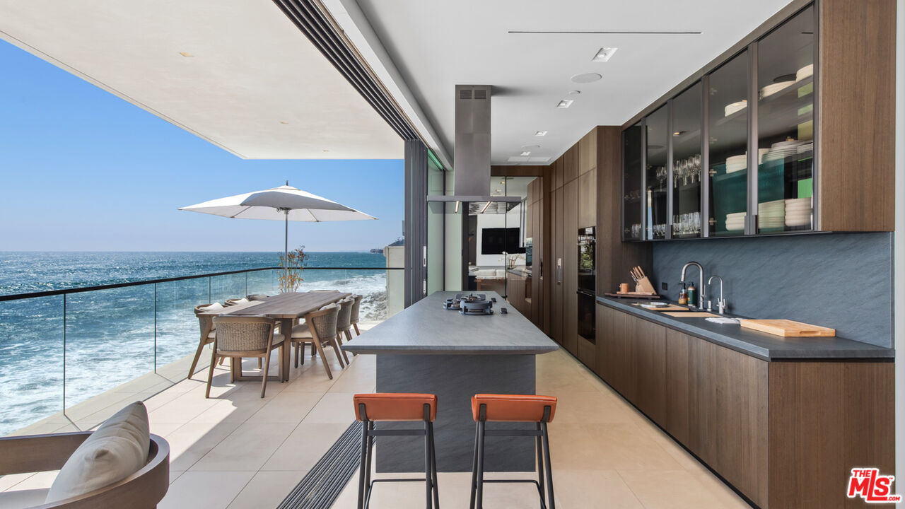 18954 Pacific Coast Highway Malibu, CA 90265 - Photo 13 of 70 a kitchen with stainless steel appliances kitchen island granite countertop a table chairs and a wooden cabinets