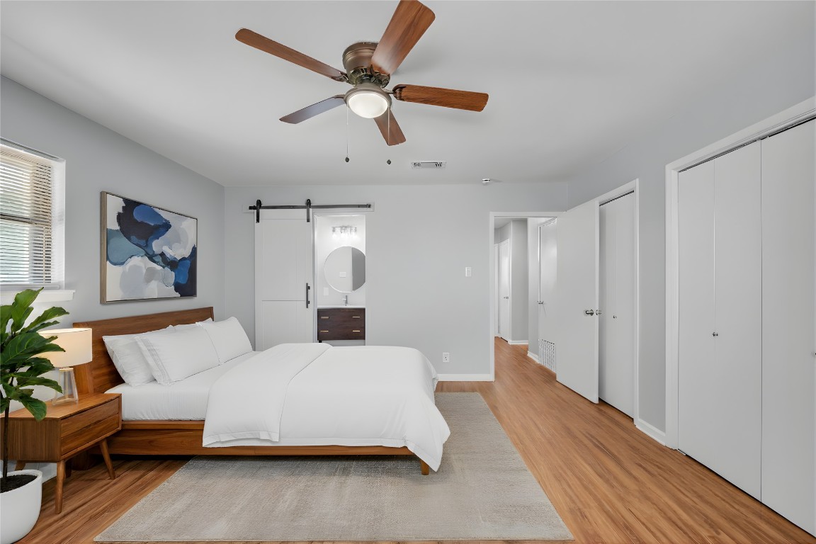 310 Hruskaville Road Temple, TX 76501 - Photo 12 of 21 Bedroom with a barn door, two closets, a ceiling fan, wood finished floors, and ensuite bathroom