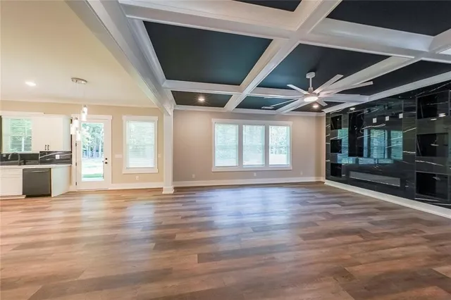 a view of an empty room with wooden floor and a kitchen