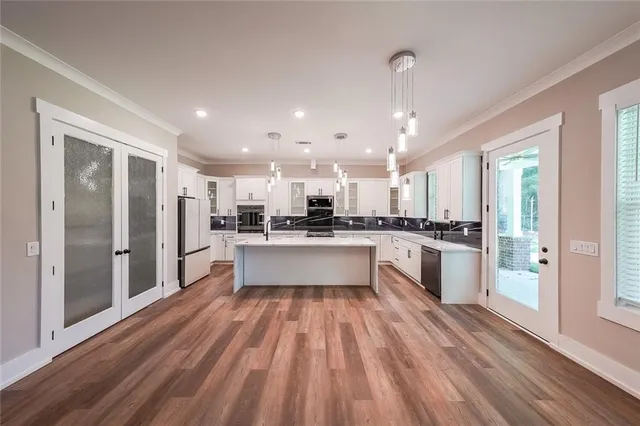 a large white kitchen with stainless steel appliances granite countertop a refrigerator a sink dishwasher a stove and white cabinets with wooden floor