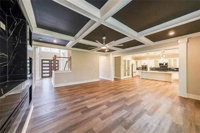 a view of an empty room with wooden floor and a kitchen view