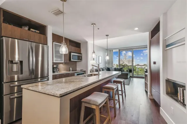 a kitchen with stainless steel appliances granite countertop a kitchen island a stove a refrigerator a oven a sink and a dining table with wooden floor