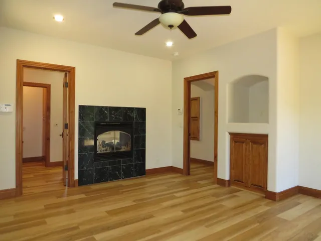 a view of an empty room with wooden floor and a ceiling fan