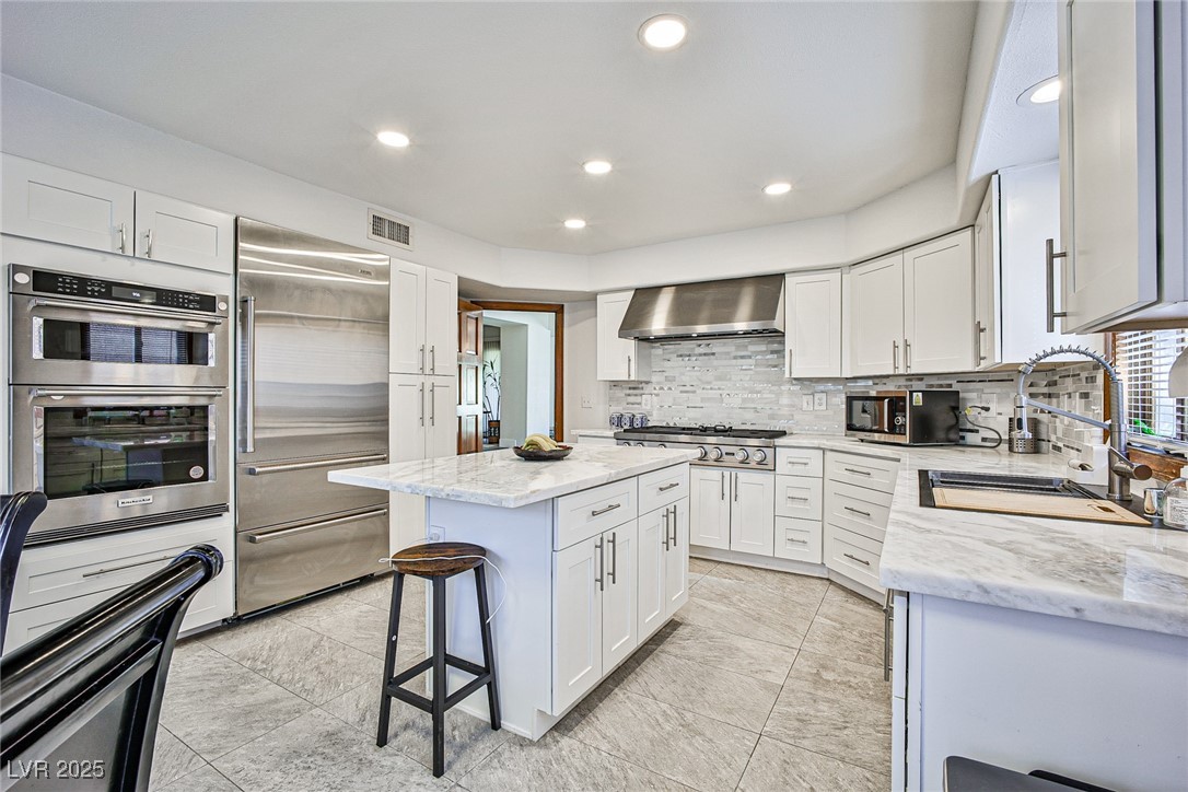 7772 Boca Raton Drive Las Vegas, NV 89113 - Photo 12 of 40 Kitchen featuring stainless steel appliances, light stone counters, white cabinets, a kitchen bar, and recessed lighting