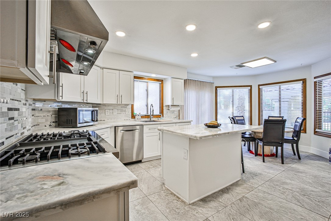 7772 Boca Raton Drive Las Vegas, NV 89113 - Photo 13 of 40 Kitchen featuring decorative backsplash, a kitchen island, range hood, white cabinetry, and stainless steel appliances