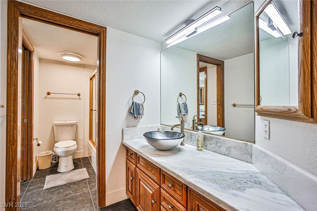 7772 Boca Raton Drive Las Vegas, NV 89113 - Photo 35 of 40 Full bathroom featuring a textured ceiling, a textured wall, vanity, dark tile patterned floors, and bath / shower combo with glass door