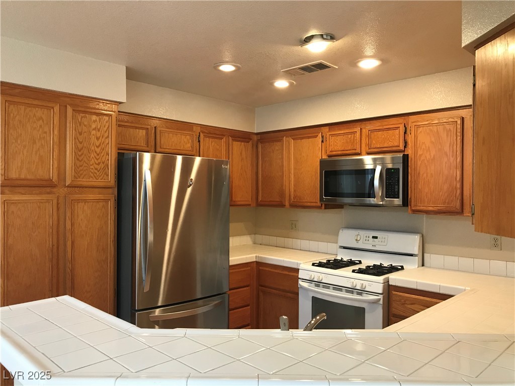 5155 West Tropicana Avenue, Unit 1155 Las Vegas, NV 89103 - Photo 4 of 11 Kitchen with tile counters, appliances with stainless steel finishes, brown cabinetry, recessed lighting, and a textured ceiling