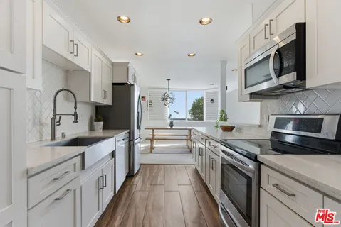 a kitchen with stainless steel appliances a sink dishwasher a stove top oven a refrigerator with wooden cabinets and floor