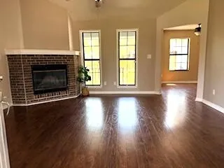 an empty room with wooden floor fireplace and windows