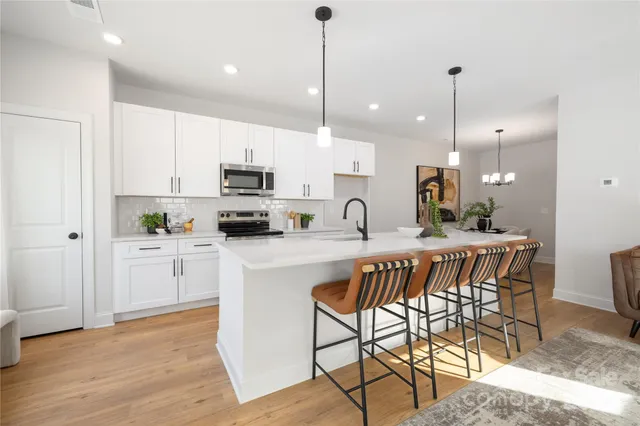 a kitchen with stainless steel appliances granite countertop a stove a sink a microwave a refrigerator with white cabinets and wooden floor