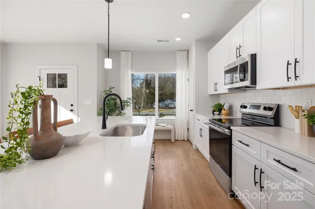 a large white kitchen with stainless steel appliances kitchen island granite countertop a lot of counter space and wooden floors
