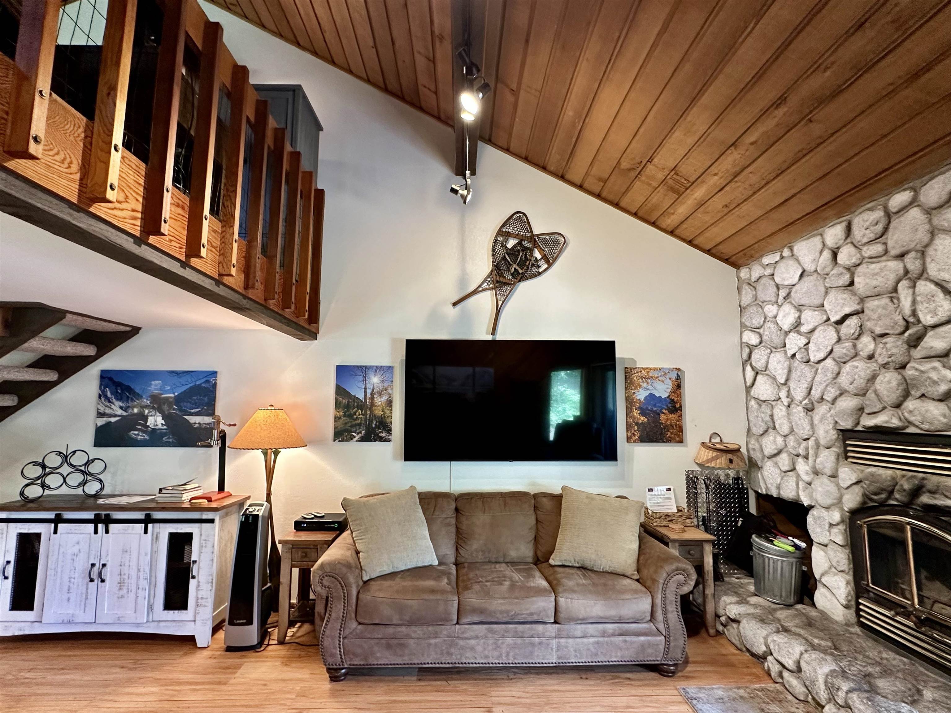 315 Fascination, Unit 315 Mammoth Lakes, CA 93546 - Photo 38 of 44 Living area featuring a stone fireplace with hearth, wood-finish flooring, a vaulted wood-plank ceiling, and a wood balcony with decorative balusters