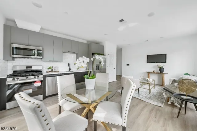 a kitchen with stainless steel appliances kitchen island granite countertop a sink a stove a dining table and chairs with wooden floor