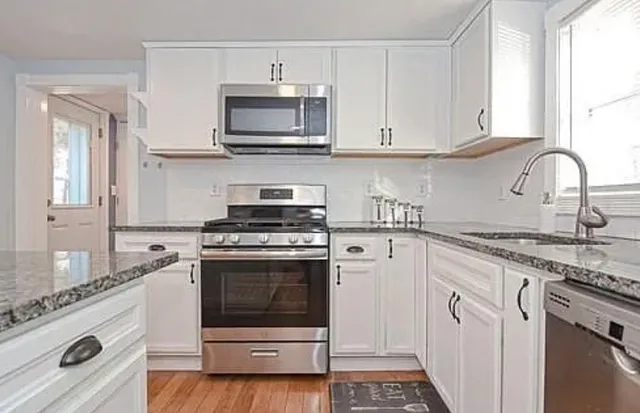 a kitchen with stainless steel appliances granite countertop grey cabinets a stove a sink and dishwasher