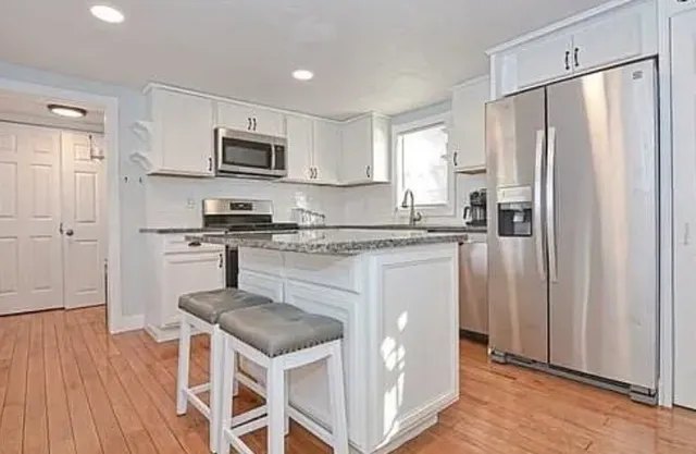 a kitchen with stainless steel appliances granite countertop a stove a sink dishwasher a refrigerator and white cabinets with wooden floor