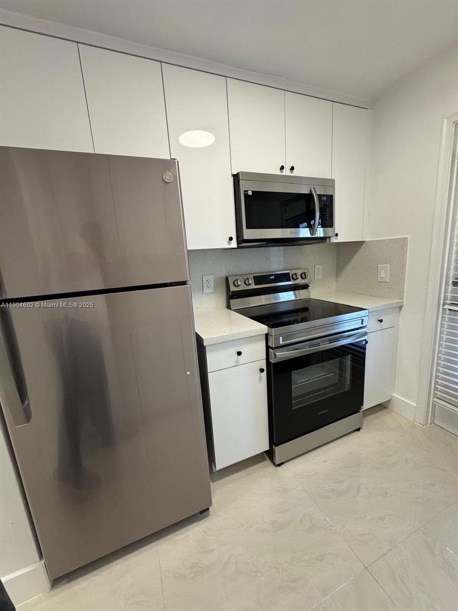 2418 Polk Street, Unit 104 Hollywood, FL 33020 - Photo 5 of 16 a kitchen with stainless steel appliances a refrigerator stove and white cabinets