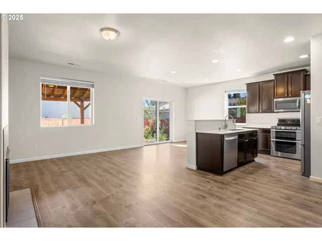 a view of kitchen with stainless steel appliances granite countertop a stove top oven a sink dishwasher and a refrigerator with wooden floor