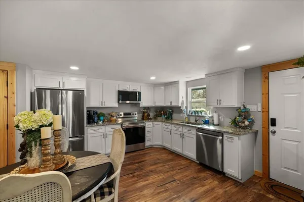 a kitchen with stainless steel appliances kitchen island granite countertop a refrigerator a stove a sink dishwasher a dining table and chairs with wooden floor