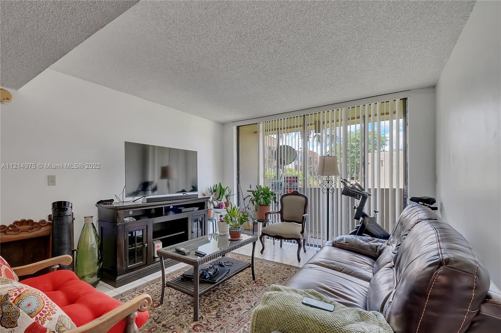 8002 Southwest 149th Avenue, Unit B201 Miami, FL 33193 - Photo 4 of 18 a living room with furniture a flat screen tv and a floor to ceiling window
