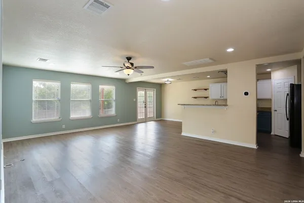 a view of an empty room with wooden floor and a kitchen