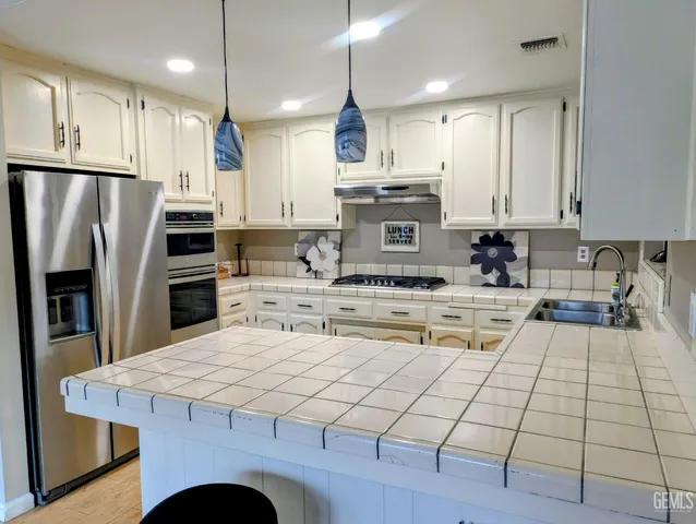 a kitchen with kitchen island granite countertop a stove a sink a refrigerator and white cabinets with wooden floor