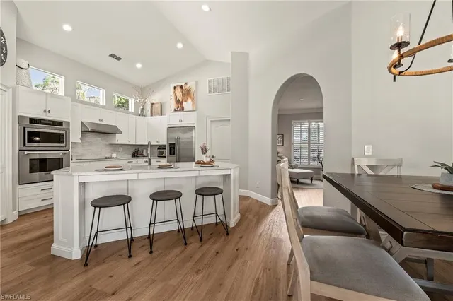 a kitchen with stainless steel appliances granite countertop a stove a sink a refrigerator and white cabinets with wooden floors