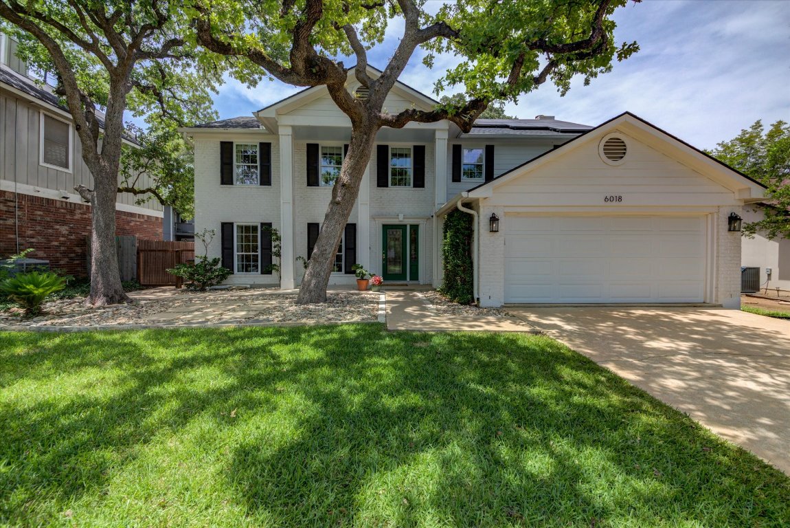 a view of a white house next to a yard with a large tree