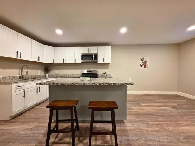 a kitchen with stainless steel appliances granite countertop a stove a sink a microwave a refrigerator and white cabinets