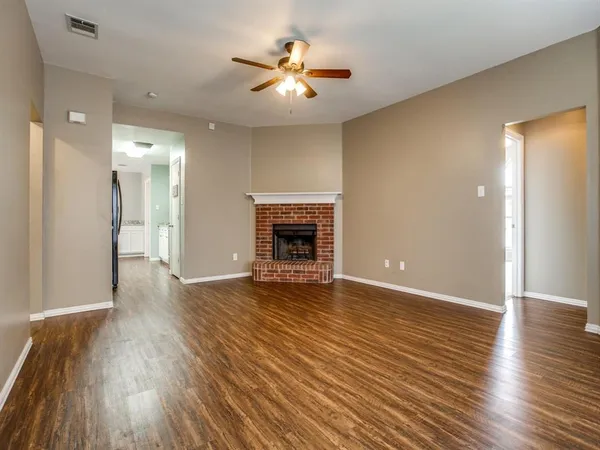 a view of an empty room with wooden floor and a fireplace