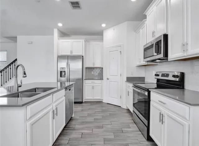 a kitchen with stainless steel appliances granite countertop white cabinets a sink a stove and a refrigerator