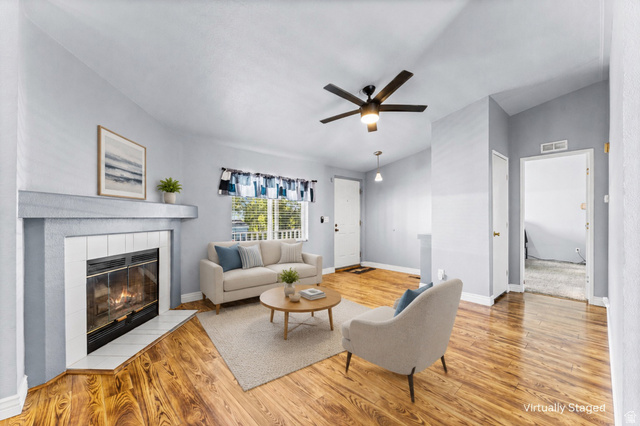 Living area featuring wood-finish flooring, a fireplace with a tiled surround, a ceiling fan, and a front entry door with a window