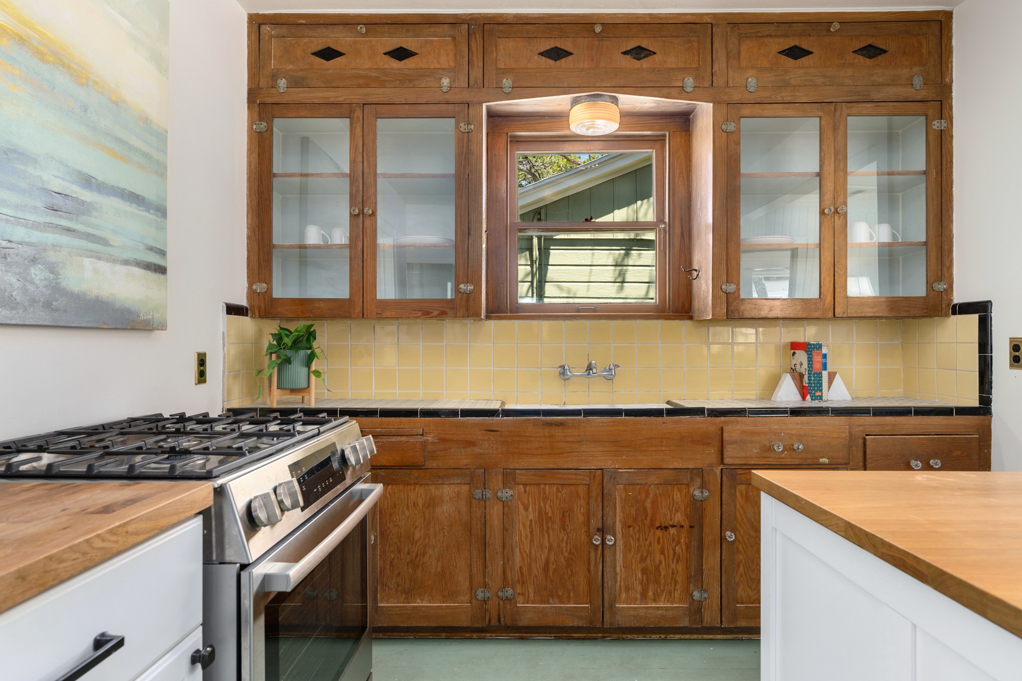 3909 Becker Avenue Austin, TX 78751 - Photo 11 of 38 Dual tone kitchen with stainless steel gas range, wood counters, glass fronted cabinets, backsplash, and two tone cabinetry