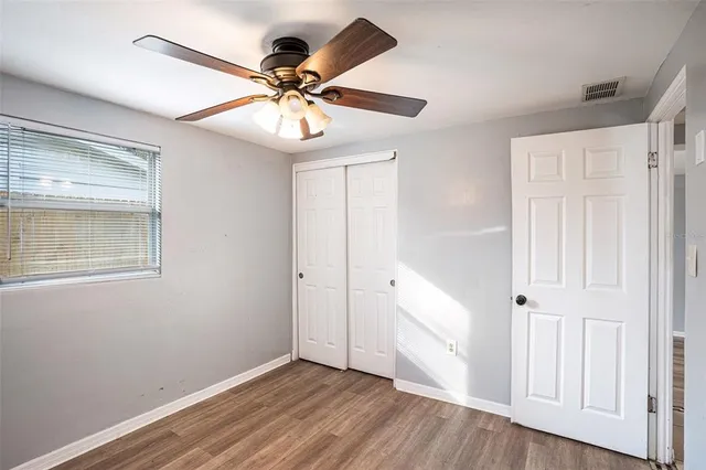 an empty room with wooden floor fan and windows