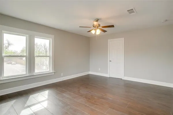 an empty room with wooden floor fan and windows