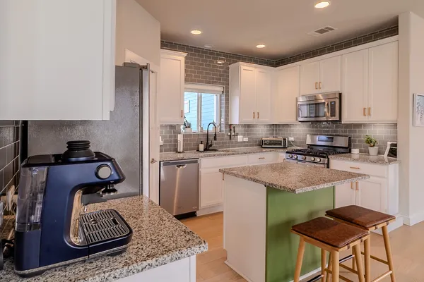 a kitchen with stainless steel appliances granite countertop a stove top oven a sink a refrigerator and white cabinets