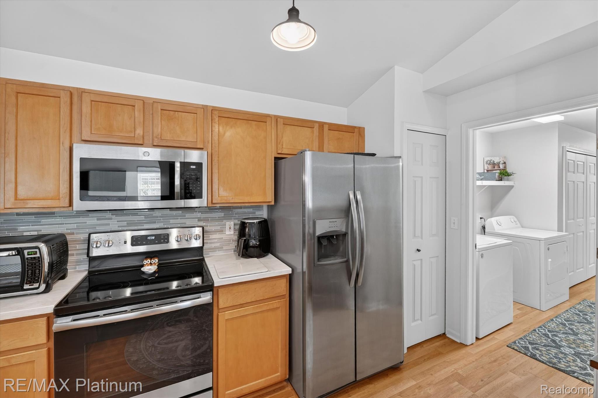 4191 Hampton Ridge Boulevard, Unit 41 Howell, MI 48843 - Photo 7 of 23 Kitchen featuring stainless steel appliances, washing machine and clothes dryer, light wood-style flooring, backsplash, and hanging light fixtures
