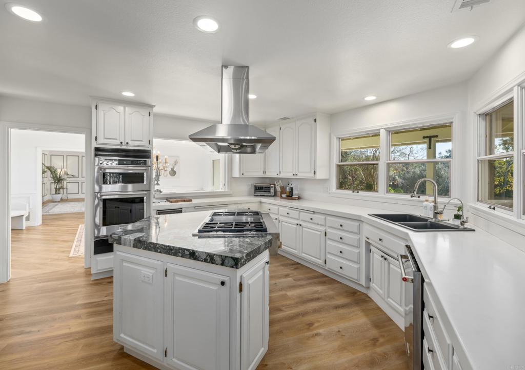9 Country Glen Road Fallbrook, CA 92028 - Photo 7 of 74 a kitchen with stainless steel appliances granite countertop a stove top oven a sink dishwasher a dining table and chairs with wooden floor