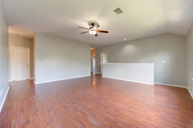 a view of an empty room with wooden floor and a ceiling fan