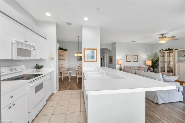a large white kitchen with kitchen island a stove a sink a refrigerator and white cabinets with wooden floor