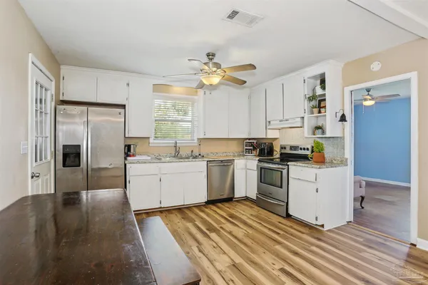a kitchen with granite countertop a refrigerator oven a sink dishwasher and white cabinets with wooden floor