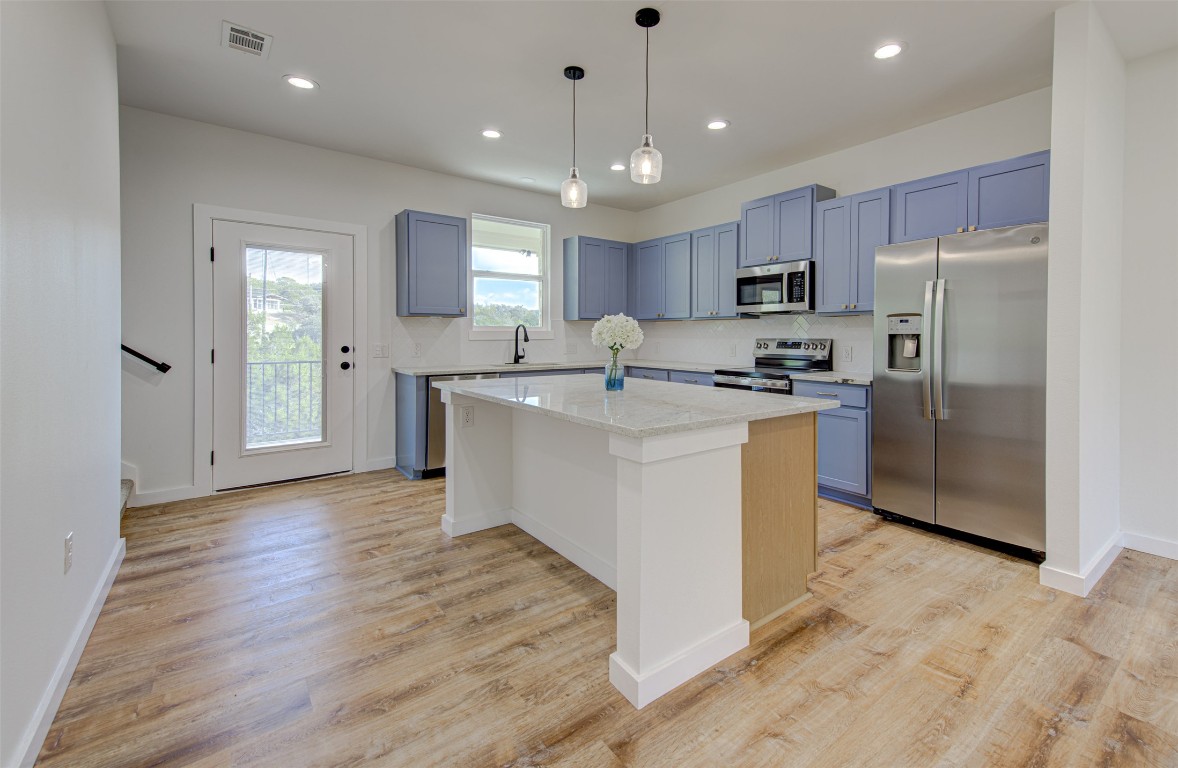 18414 Roundrock Road Jonestown, TX 78645 - Photo 4 of 30 Kitchen with stainless steel appliances, a center island, pendant lighting, light stone counters, and recessed lighting
