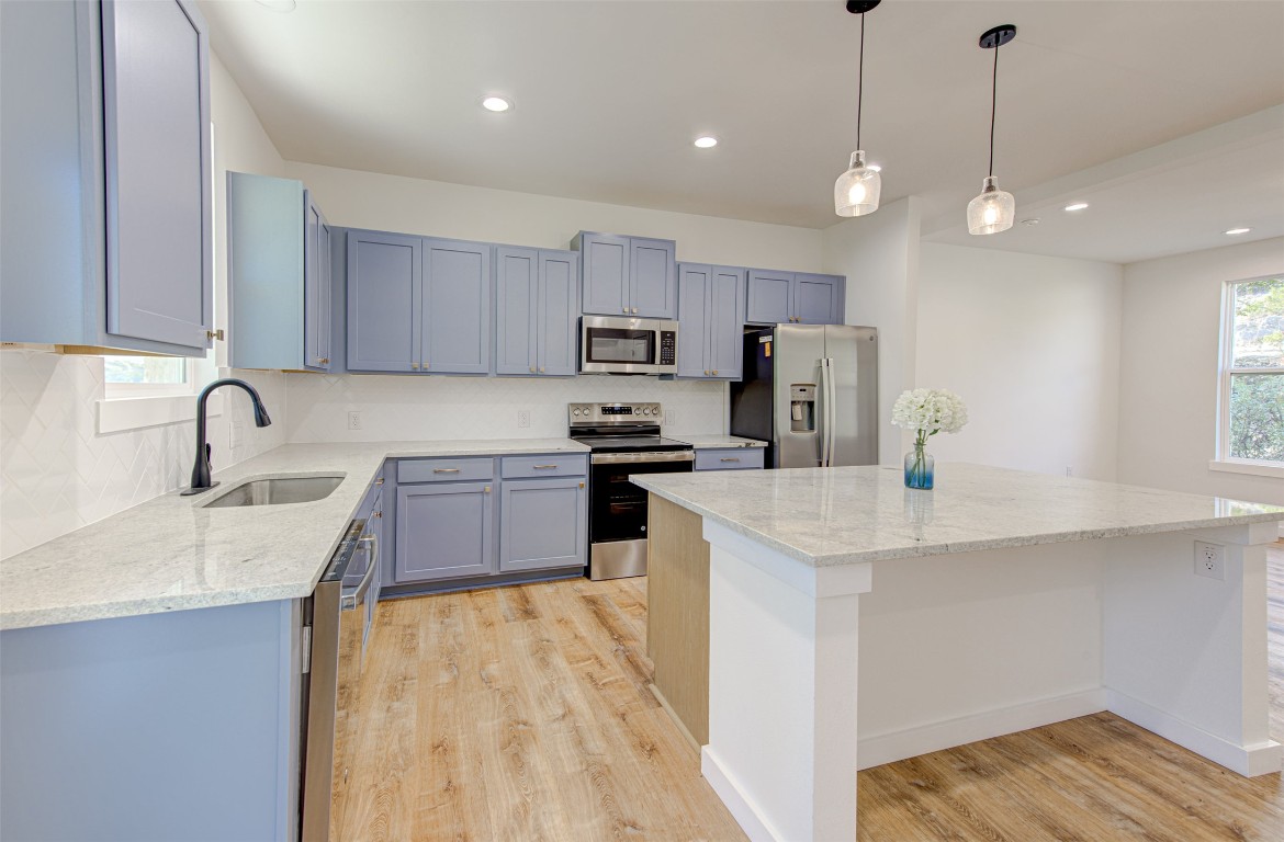 18414 Roundrock Road Jonestown, TX 78645 - Photo 5 of 30 Kitchen featuring light stone counters, stainless steel appliances, decorative light fixtures, a center island, and light wood-style floors