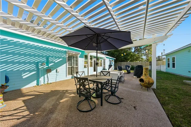 a view of a patio with table and chairs under an umbrella with a barbeque